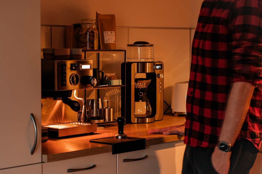 Person standing beside a home espresso machine and grinder.