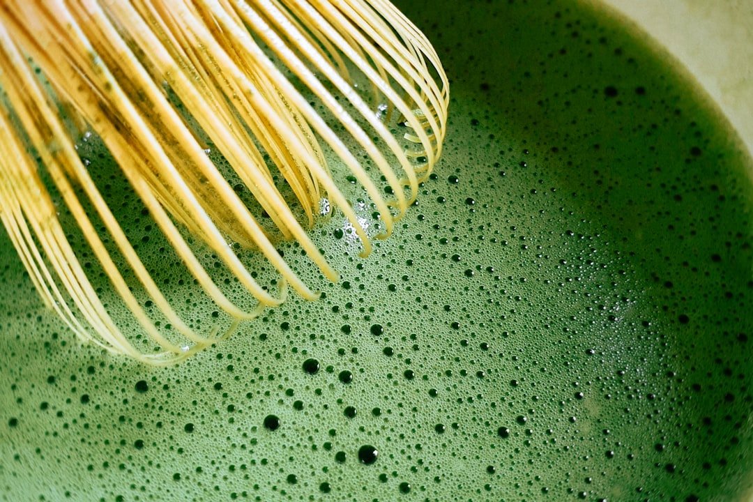 Close-up of a bamboo whisk over foamy green matcha.