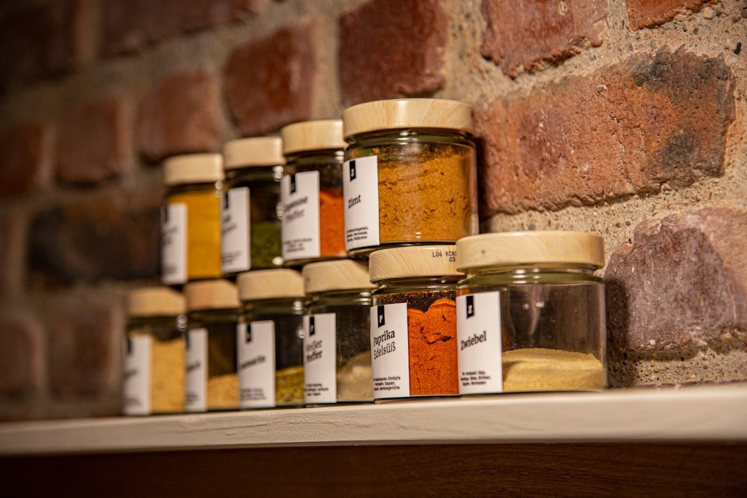 Glass jars and flavor supplies arranged on a wooden kitchen shelf.